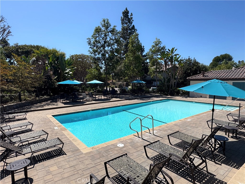 Resort-style community pool with sun loungers, turquoise umbrellas, and lush landscaping. - 29 Waxwing, Aliso Viejo CA 92656 - photo 28