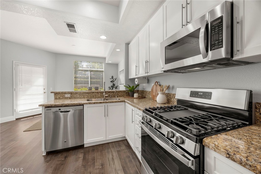 Granite countertops, white cabinetry, stainless steel appliances, a gas range, and an open-concept design create a kitch - 66 Cinnamon Teal, Aliso Viejo CA 92656 - photo 13