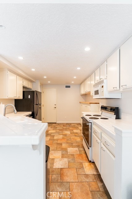 Bright galley-style kitchen with abundant cabinetry, recessed lighting, and included appliances. - 2154 San Michel Dr W #A, Costa Mesa CA 92627 - photo 1