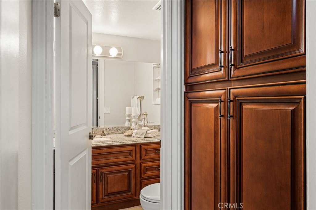 Stylish powder room featuring a granite-topped wood vanity and decorative glass-front wall cabinet. - 12632 Romaine Wy, Garden Grove CA 92845 - photo 25