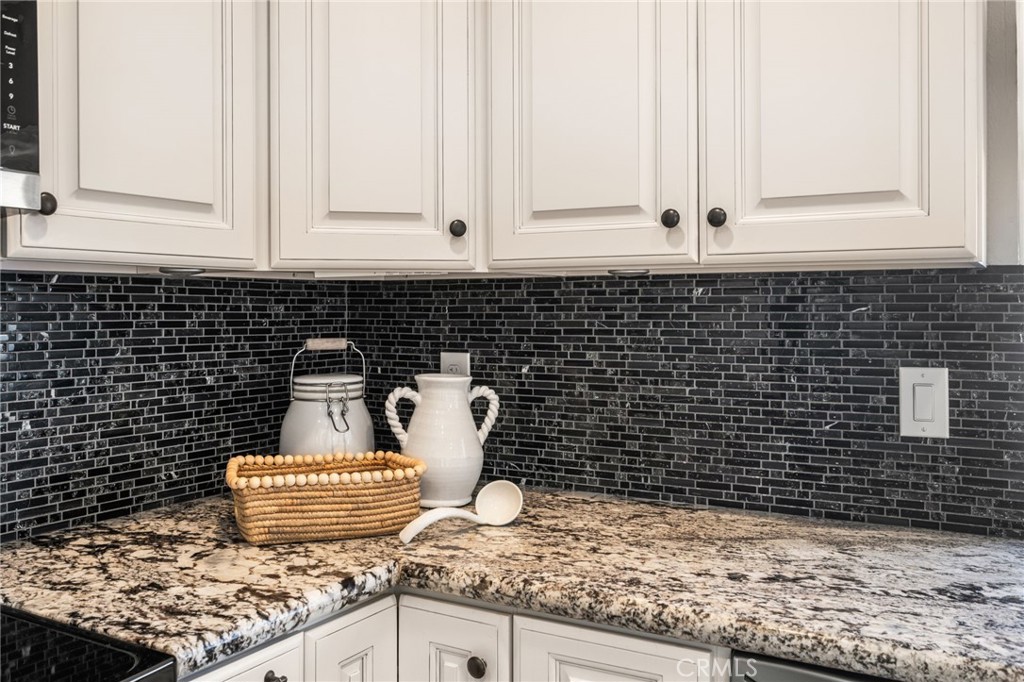 Richly patterned granite and a contrasting mosaic backsplash complement the classic white cabinetry. - 6931 Danvers Dr, Garden Grove CA 92845 - photo 20