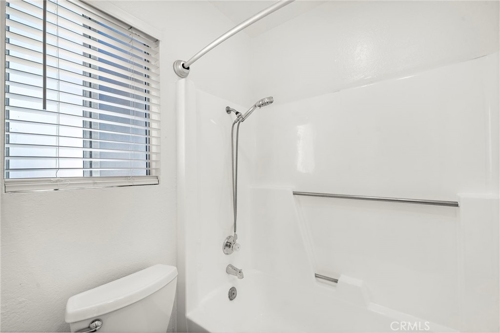 The bright tub-and-shower area features a window, white surround, and a handheld showerhead. - 9941 11th Street, Garden Grove CA 92844 - photo 28