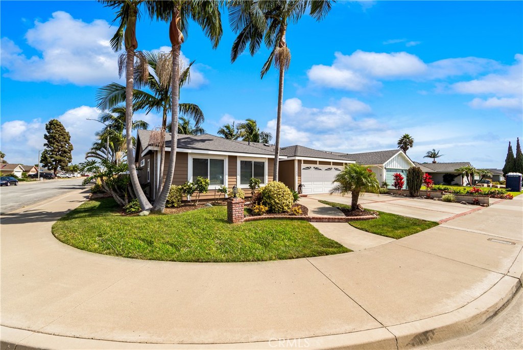 Front exterior featuring mature palm trees, landscaped grounds, and generous driveway space. - 17042 Friml Lane, Huntington Beach CA 92649 - photo 3