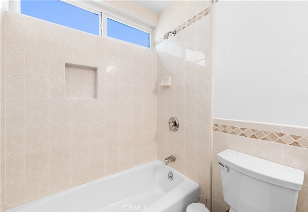 Guest bathroom tub and shower area with a clean, neutral tile surround. - 17042 Friml Lane, Huntington Beach CA 92649 - photo 28