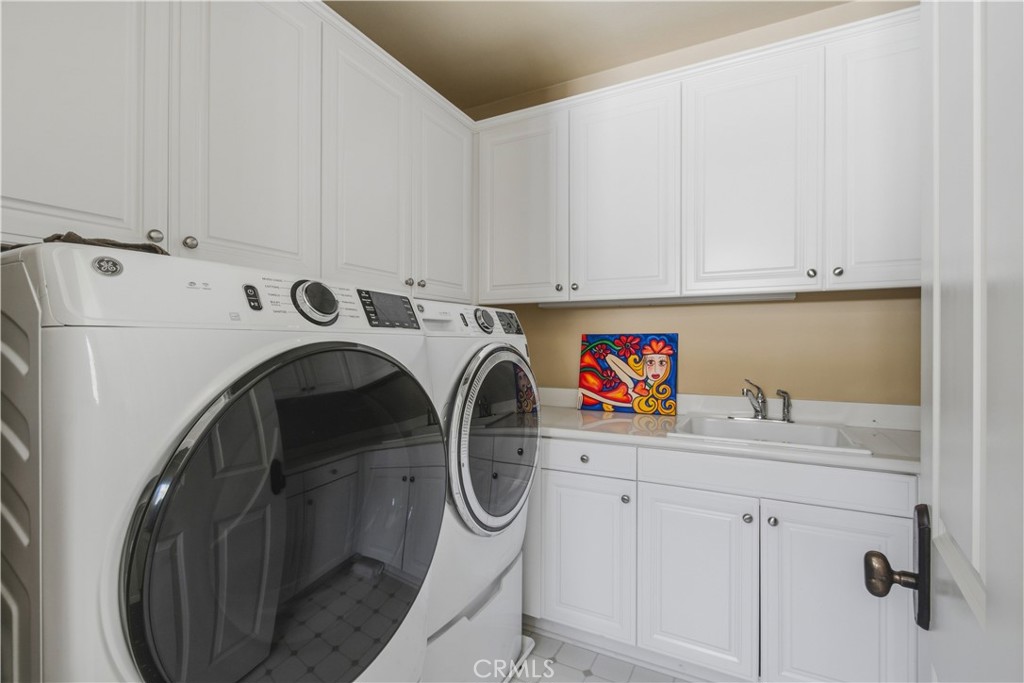 Upper-level laundry room includes side-by-side washer and dryer, upper and lower cabinetry for storage, utility sink wit - 21322 Balerma, Huntington Beach CA 92648 - photo 29