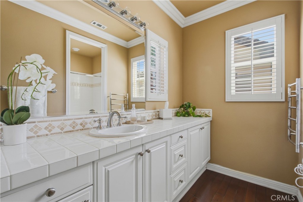 Upper-level 3rd Ensuite bathroom including white vanity with cabinetry, tile countertop, sink, large mirror, overhead va - 21322 Balerma, Huntington Beach CA 92648 - photo 38