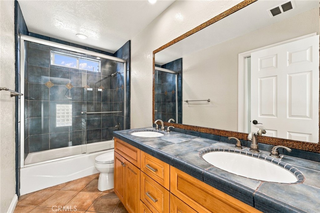 Hall bathroom features a dual-sink vanity, tile flooring, tub/shower, tiled walls, and glass enclosure. - 803 Frankfort Avenue, Huntington Beach CA 92648 - photo 51
