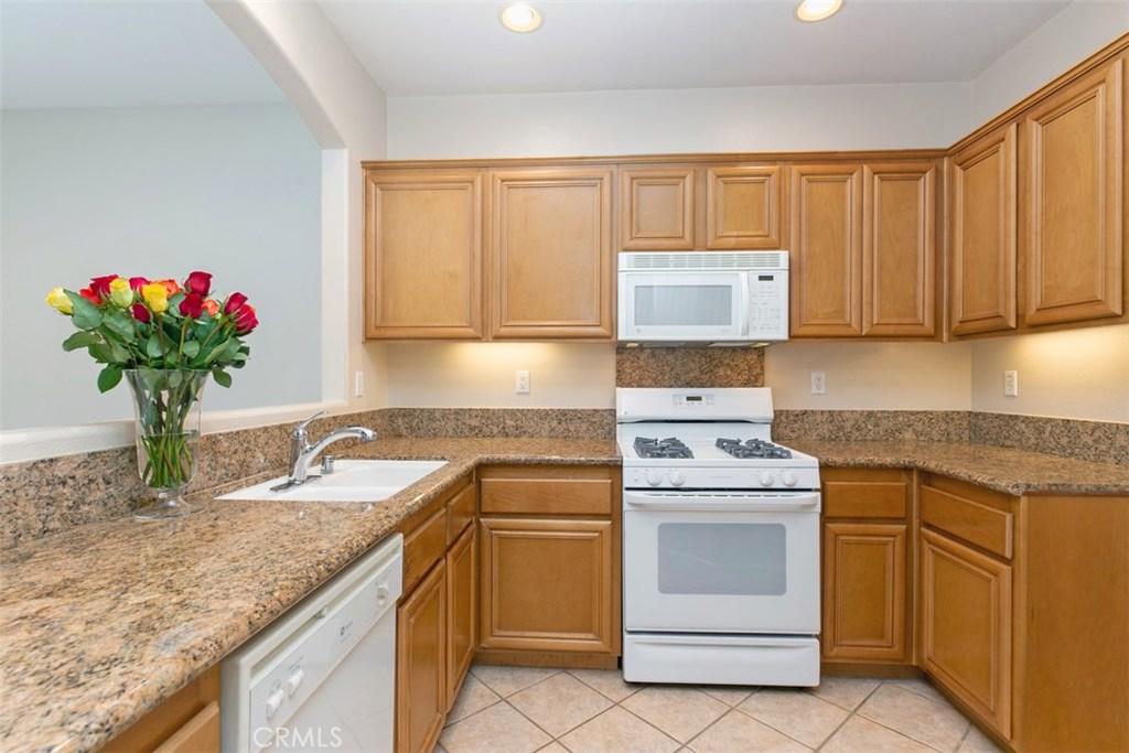Wraparound kitchen with slab granite countertops, maple cabinets, and white appliances. *flooring to be updated with LVP - 10 New Market, Irvine CA 92602 - photo 8