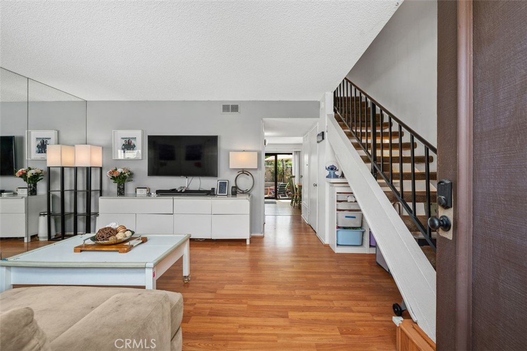 Living room with laminate wood-look flooring, staircase, and hallway leading to the kitchen and dining area. - 14 Greenleaf, Irvine CA 92604 - photo 3