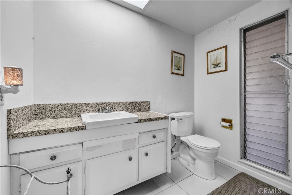 Guest bathroom with granite countertops, white vanity cabinetry, tile flooring, and a skylight. - 919 Glencliff, La Habra CA 90631 - photo 13
