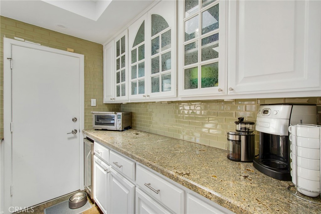 View of white cabinetry with decorative glass-front accents, granite countertops, glass tile backsplash and side door en - 31731 Seacove, Laguna Beach CA 92651 - photo 39