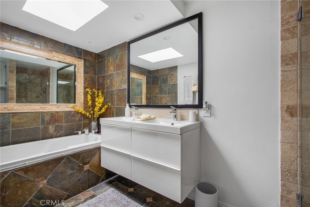 View of Guest bathroom with deep soaking tub with natural stone tile, vanity, mirrors, recessed lighting, and a skylight - 31731 Seacove, Laguna Beach CA 92651 - photo 44