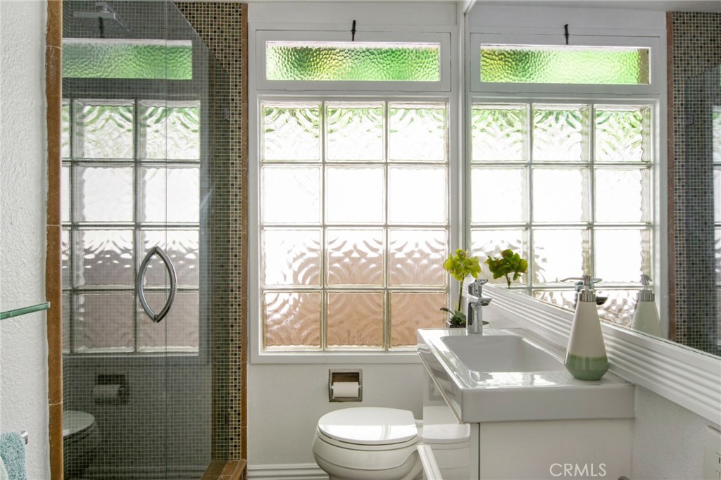Guest bathroom view of glass block windows, modern sink, large vanity mirror and glass doors into tiled walk-in shower. - 31731 Seacove, Laguna Beach CA 92651 - photo 48