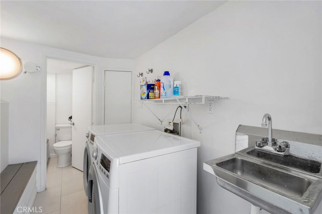 Laundry room featuring side-by-side washer and dryer, utility sink, storage shelving, and direct access to an adjacent h - 31731 Seacove, Laguna Beach CA 92651 - photo 50