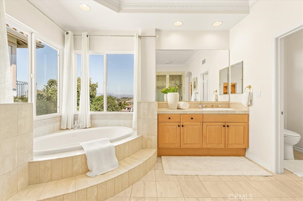 A luxurious primary bath with a tiered soaking tub, expansive windows, and captivating hillside views. - 28932 Drakes Bay, Laguna Niguel CA 92677 - photo 54