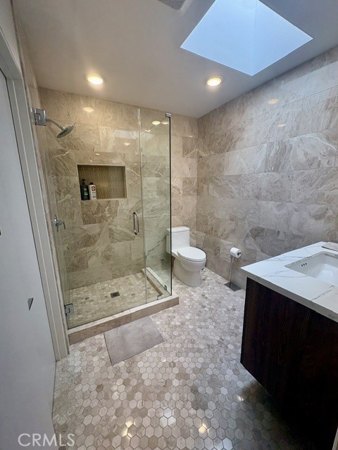 Primary bathroom has gorgeous tile flooring, stone walls, skylight and shower with accessory shelf. - 3386 Punta Alta A, Laguna Woods CA 92637 - photo 20