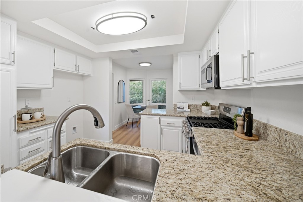 Kitchen with stainless double sink, granite counters and white cabinets. - 25911 Blascos 102, Mission Viejo CA 92691 - photo 16