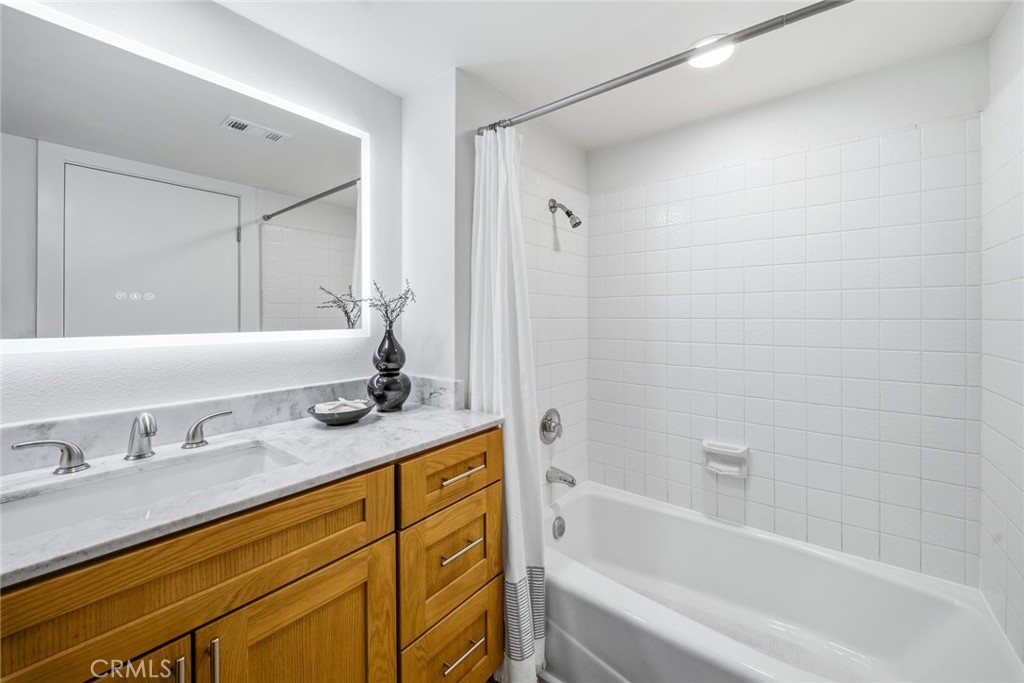 Bathroom with backlit mirror, wood vanity and tub/shower. - 25911 Blascos 102, Mission Viejo CA 92691 - photo 24