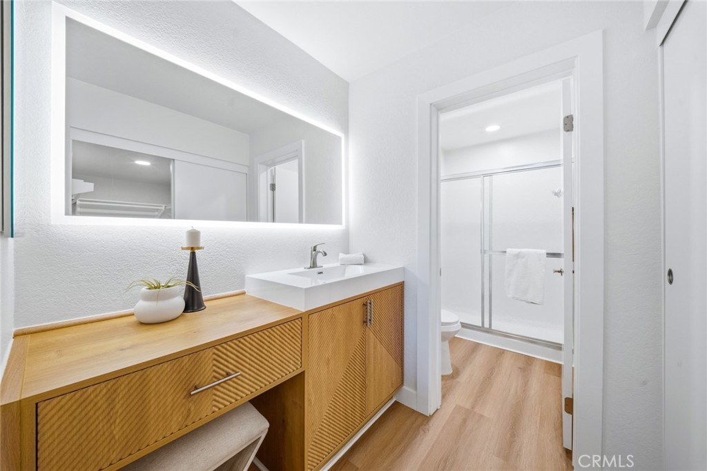 Bathroom with long wood vanity, backlit mirror and stall shower beyond. - 25911 Blascos 102, Mission Viejo CA 92691 - photo 26