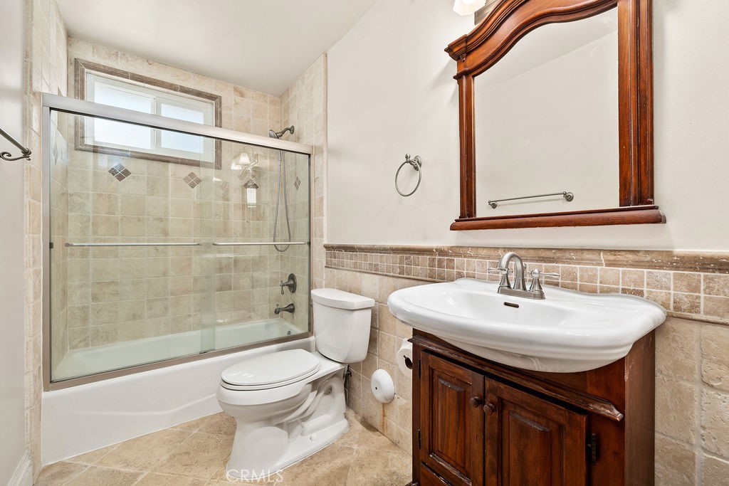 Bathroom features travertine-style tile flooring and surround, tiled shower walls, and a wood vanity. - 150 S Park, Orange CA 92869 - photo 19