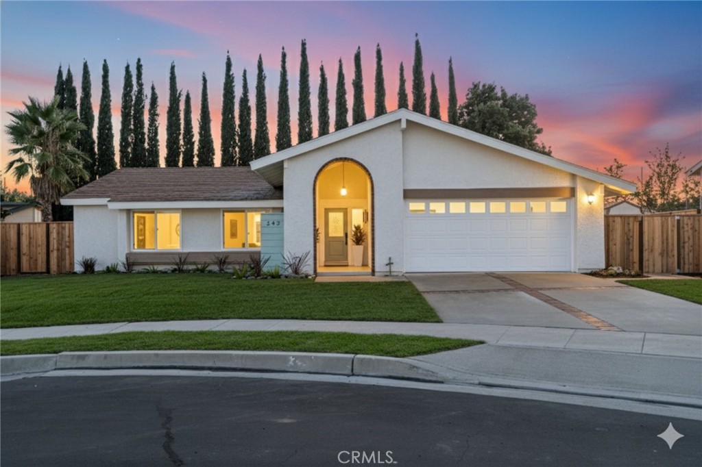 Evening curb appeal with the arched entry aglow, brick-ribbon driveway, fresh landscaping, and cul-de-sac setting under - 242 E Paddle Wheel, Orange CA 92865 - photo 1