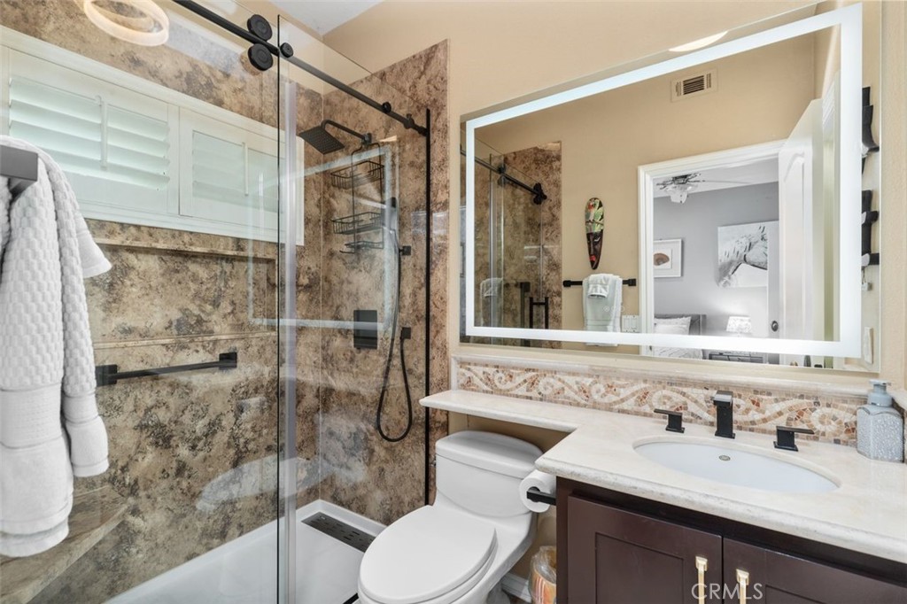This beautifully updated ensuite bath features a step in shower with richly veined stone tile, a sleek sliding glass enc - 21792 Hermosa Lane, Rancho Santa Margarita CA 92679 - photo 22