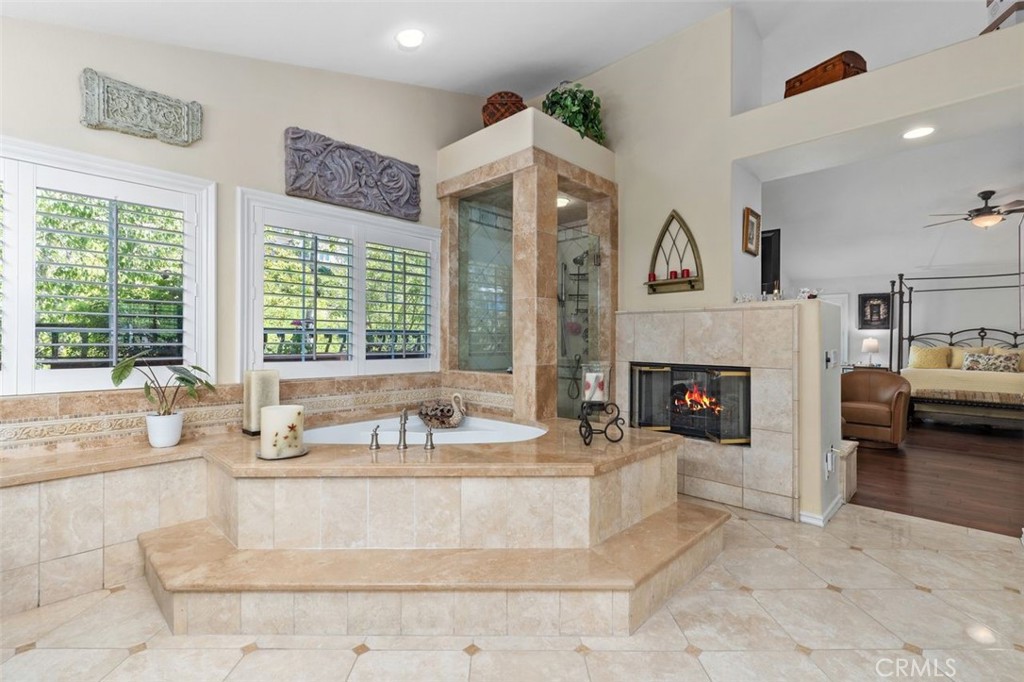 The spa like primary bath features a soaking tub with travertine surround, a glass enclosed shower, and a two sided fire - 21792 Hermosa Lane, Rancho Santa Margarita CA 92679 - photo 28