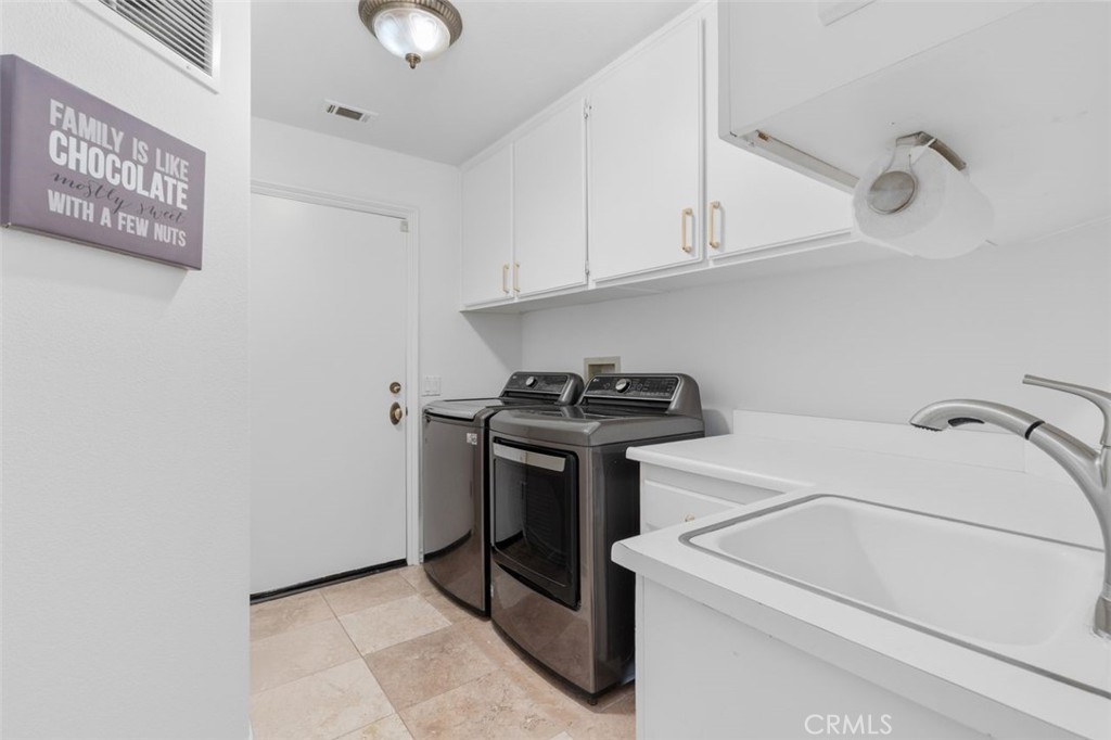 The spacious indoor laundry room features a utility sink, white cabinetry with gold hardware, travertine tile floors, an - 21792 Hermosa Lane, Rancho Santa Margarita CA 92679 - photo 37