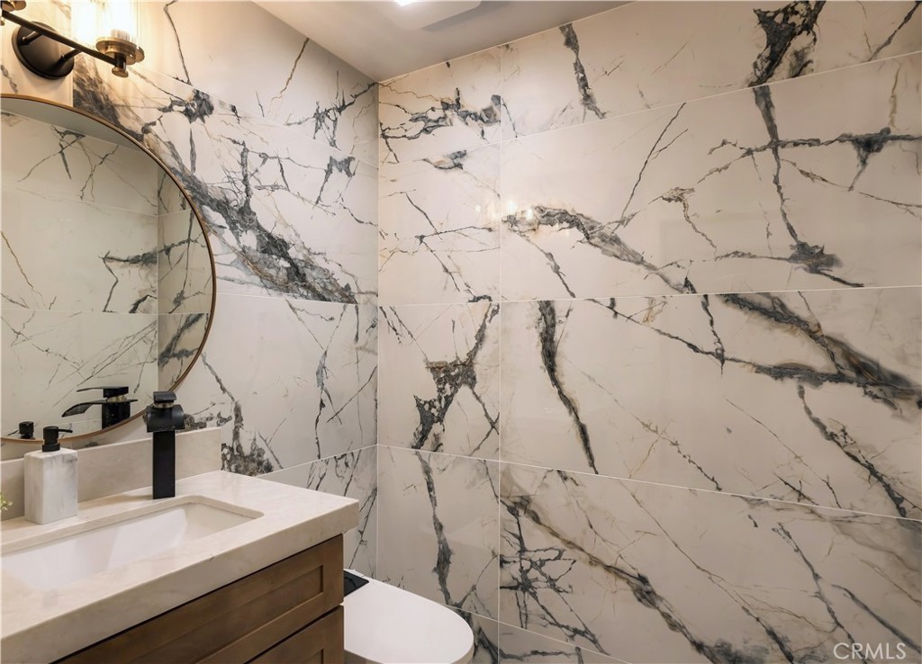 Powder Room: Dramatically veined stone wraps the walls, finished with a round brass mirror and waterfall faucet. - 126 Calle Redondel, San Clemente CA 92672 - photo 31