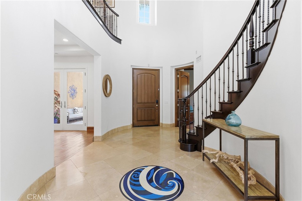 Elegant entry hall with curved staircase, travertine floors, custom iron railing, oversized front door, and dramatic dou - 31491 Carril De Maderas, San Juan Capistrano CA 92675 - photo 5