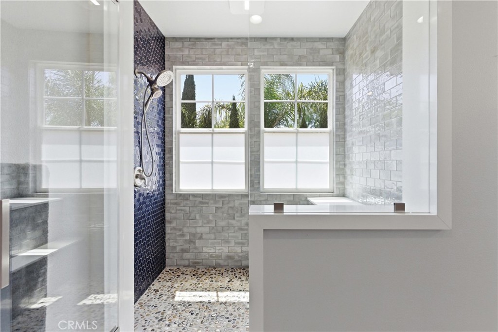Spa-inspired primary bathroom featuring a frameless walk-in shower, designer tilework, pebble stone flooring, and abunda - 31491 Carril De Maderas, San Juan Capistrano CA 92675 - photo 51