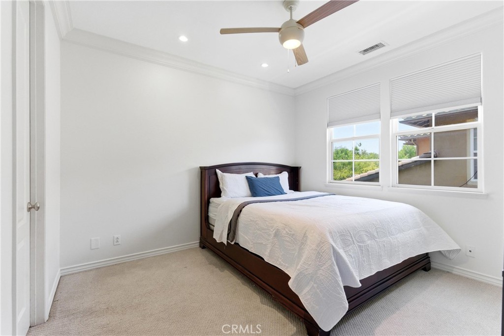 Spacious upstairs bedroom with plush carpeting, crown molding, ceiling fan, and oversized windows. - 31491 Carril De Maderas, San Juan Capistrano CA 92675 - photo 57